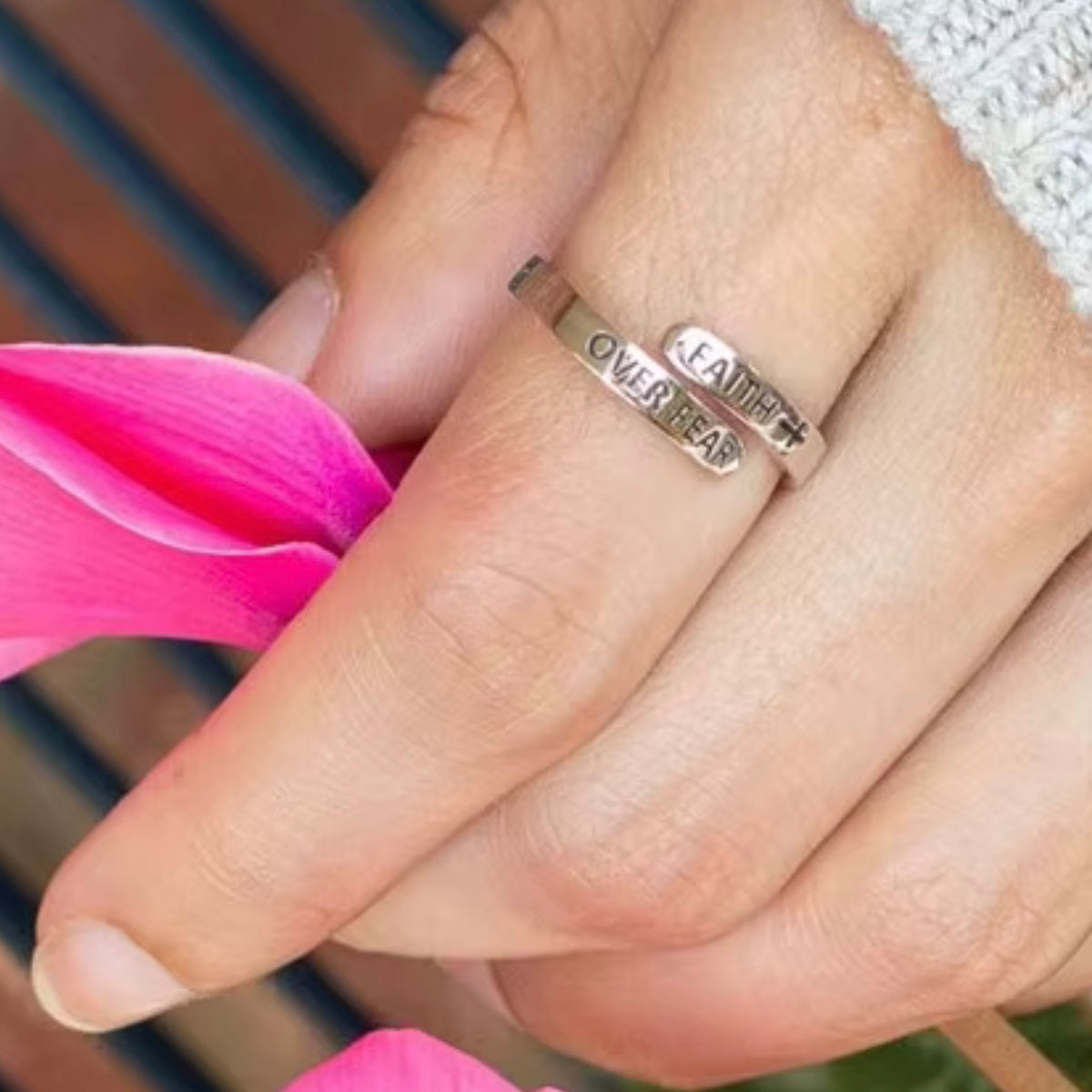 Silver-tone Faith Over Fear ring worn beside a pink flower
